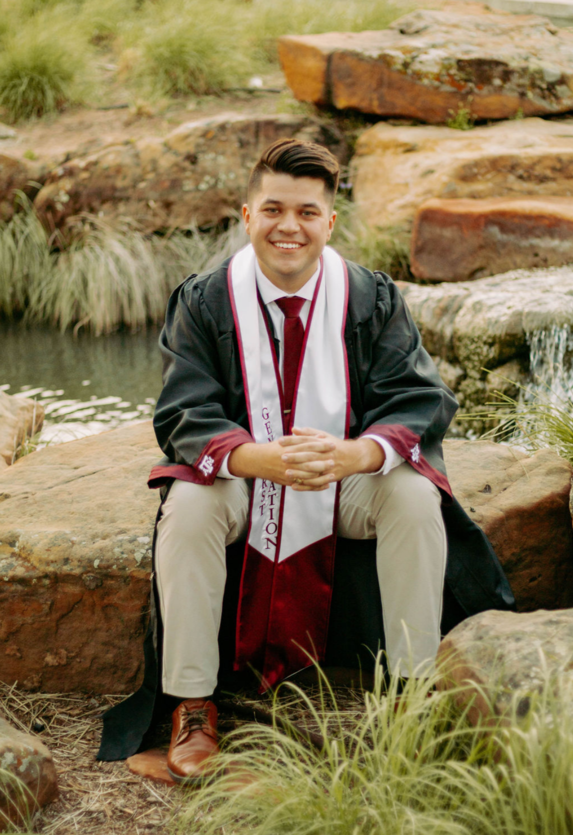 Braden Farrell wearing Texas A&M graduation regalia by a campus pond